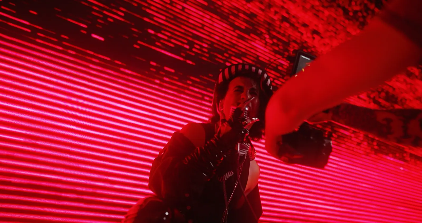 A rapper under red light lines, shot from below with the camera in frame